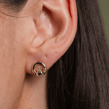 Gold earring worn on a person's ear with a neutral background