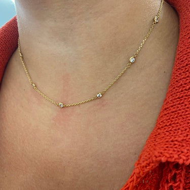 Gold necklace with small green gemstones worn by a person in an orange sweater.