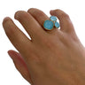 Hand wearing a ring with three turquoise stones on a white background