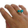 Turquoise gemstone ring with gold band on a hand against a white background