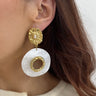 Close-up of a woman wearing gold and white earrings with a neutral background