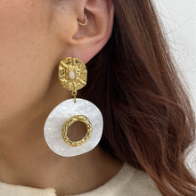 Close-up of a woman wearing gold and white earrings with a neutral background