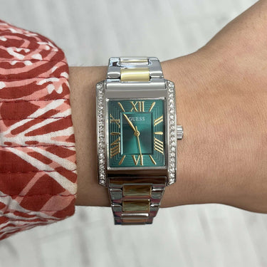 Person wearing a silver watch with a green face on a neutral background
