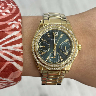 Gold wristwatch on a wrist with a patterned sleeve and blurred background