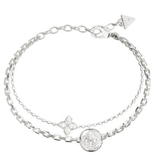A silver-toned double-strand chain bracelet featuring a circular medallion, a four-petal floral charm, and a triangular logo tag on the clasp, set against a plain white background.