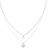 A delicate double-layered silver necklace featuring a fine chain with a small clover-shaped charm and a longer chain with a round medallion pendant, shown on a plain white background.