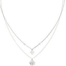 A delicate double-layered silver necklace featuring a fine chain with a small clover-shaped charm and a longer chain with a round medallion pendant, shown on a plain white background.