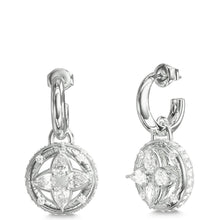 A pair of silver-toned huggie hoop earrings with circular drop charms featuring a floral quatrefoil design set with clear stones, shown from front and side angles on a white background.