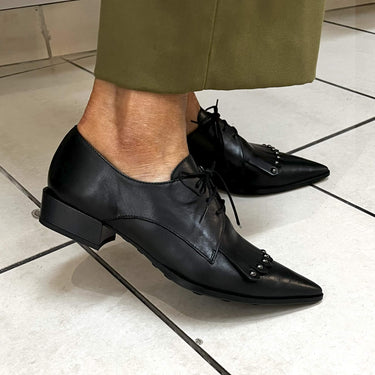 Black leather shoes worn with green pants on a tiled floor