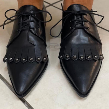 Black leather shoes with fringe details on a light background