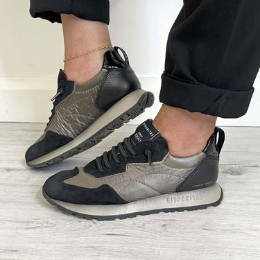 Black and gray sneakers worn by a person on a light wooden floor.
