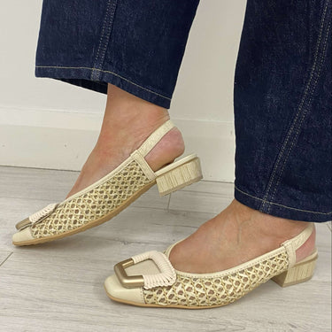 Gold woven flats worn with dark blue jeans on a light wooden floor.
