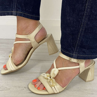 Beige high-heeled sandals worn with dark blue jeans on a light wooden floor.