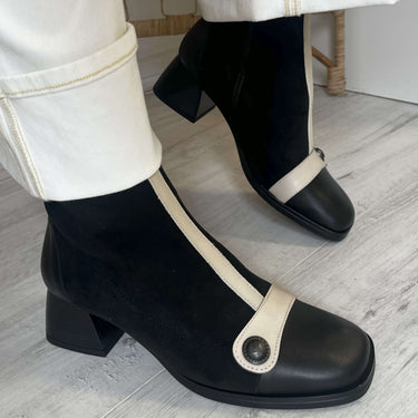 Black and white shoes worn with white pants on a light wooden floor.