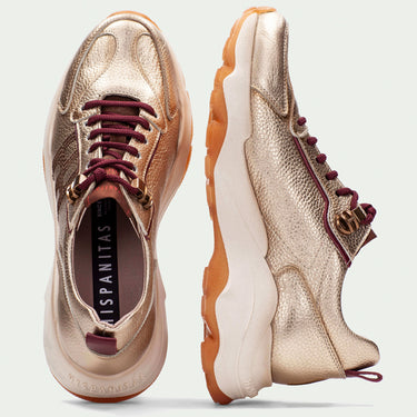 Pair of rose gold sneakers with brown soles on a light gray background