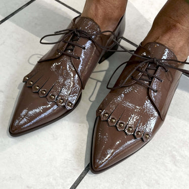 Brown patent leather shoes with decorative studs on a light background