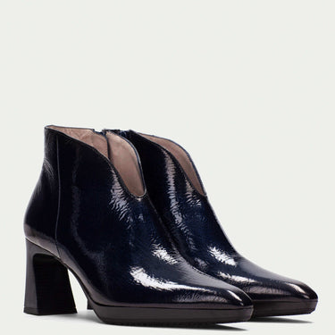 Pair of navy patent leather ankle boots on a light gray background