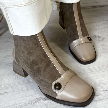Pair of brown and beige ankle boots worn with white pants on a light wooden floor.