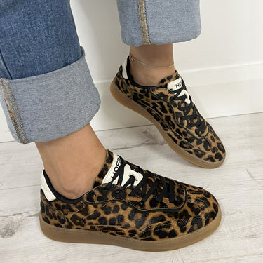 Leopard print sneakers worn with rolled-up jeans on a light wooden floor.
