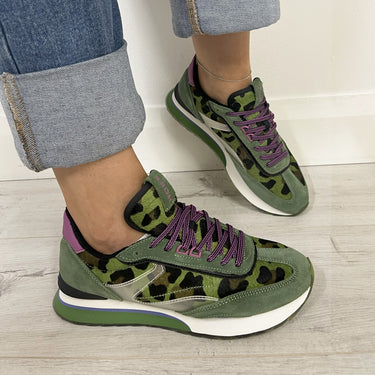 Green animal pattern sneakers with purple laces worn on a light wooden floor.