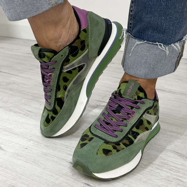 Green and purple sneakers worn with rolled-up jeans on a light wooden floor.