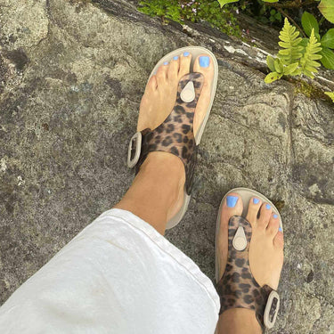 Person wearing leopard print sandals on a stone path with green plants.