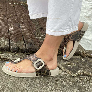 Close-up of feet wearing leopard print sandals on a stone surface.