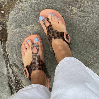 Person wearing leopard print sandals on a stone pavement