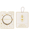 Joma Jewellery Strength affirmation card jewelry set, featuring a beaded bracelet with gold and dark brown beads, shown alongside its cream-colored packaging cards with gold celestial illustrations.