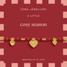 A Joma Jewellery 'A Little Cosy Season' beaded bracelet with red and gold beads and three gold heart charms, displayed on its red and pink packaging card.
