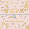 A Joma Jewellery Christmas-themed bracelet on its original pink card packaging. The bracelet is a delicate silver chain with a central silver heart charm engraved with 'I LOVE MY FAMILY'.