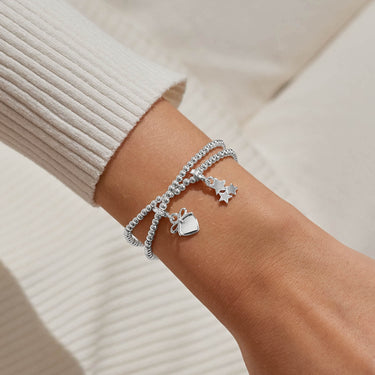 Silver bracelet with charms on a wrist against a neutral background
