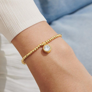 Gold bracelet with a clear gemstone on a wrist against a light background