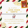 A silver beaded bracelet with a Santa Claus charm, presented on a decorative white card with Christmas-themed postage stamp designs and gold text. The brand 'Joma Jewellery' is visible at the bottom.