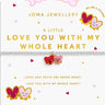 A Joma Jewellery bracelet displayed on its branded backing card. The bracelet is a delicate silver-toned chain with two small, smiling heart charms in red and pink.