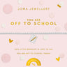 A silver beaded bracelet with a small gold and white enamel charm featuring a pencil, displayed on a light pink Joma Jewellery gift card with gold text and school-themed graphics.