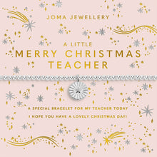 A square pink Christmas-themed card with gold and silver glittery text reading 'Joma Jewellery' and 'A Little Merry Christmas Teacher,' plus decorative stars, snowflakes, and a horizontal silver beaded bracelet centered across the middle on a white background.