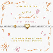 A silver beaded bracelet with a gold crescent moon and a gold heart charm engraved with 'Happy Birthday', presented on a white card with gold and pink November-themed illustrations and text from Joma Jewellery.