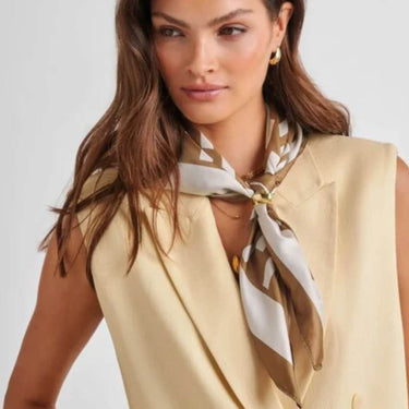 Woman wearing a beige sleeveless top with a patterned scarf around her neck against a plain background