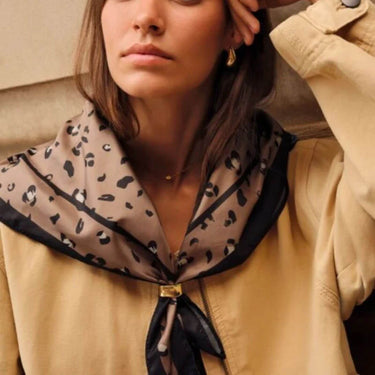 Woman wearing a beige coat with a leopard print scarf around her neck.