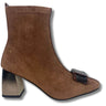 A brown suede ankle boot with a block heel and a decorative dark brown and black buckle detail on the toe, shown against a plain white background.