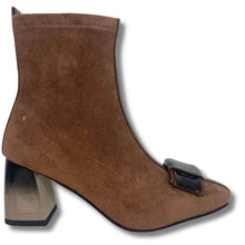 A brown suede ankle boot with a block heel and a decorative dark brown and black buckle detail on the toe, shown against a plain white background.