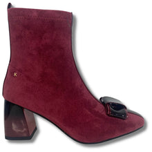 A burgundy suede ankle boot with a block heel, a glossy black decorative buckle detail on the toe, and a small gold 'K' logo on the side, shown against a plain white background.