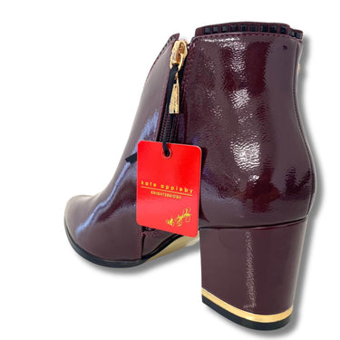 Patent leather ankle boot with a red tag on a white background