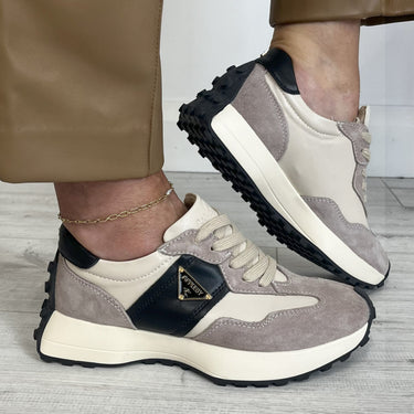 taupe and beige sneakers with black accents worn by a person on a light wooden floor.
