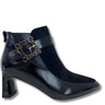 A black ankle boot with a pointed toe, block heel, and a decorative gold-tone buckle strap across the instep, shown on a white background.