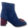 A navy blue suede ankle boot with a block heel, featuring a contrasting deep burgundy suede toe cap and a small gold metal accent on the side.