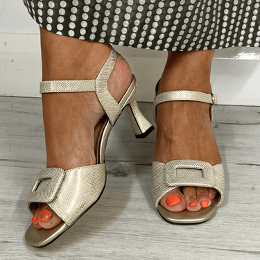 Gold high-heeled sandals worn with a polka dot skirt on a wooden floor.