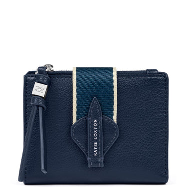 A navy blue pebbled leather card holder wallet by Katie Loxton, featuring a vertical navy and cream stripe on the front, a matching leather arrow-shaped tab with the brand name, and a leather tassel zipper pull.