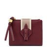A burgundy pebbled leather zip-around wallet by Katie Loxton, featuring a vertical beige and white stripe on the front, a matching leather tab with the brand name, and a gold-tone zipper pull.